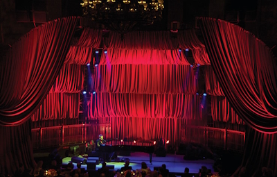 An event drape rentals setup with layered red curtains and swag drapery on stage with theatrical lighting